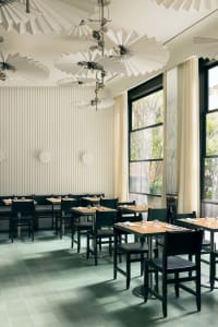 A modern restaurant with minimalist decor, featuring tables made of wood and metal, and glass elements.