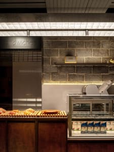 Sandwich shop with a concrete and steel interior design, featuring exposed brick walls and bright lighting.