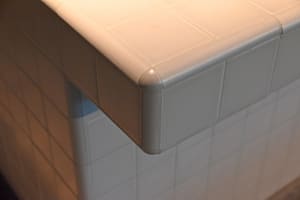 A close-up of a white tile interior wall corner with a corner protector.