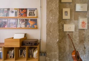 A music room with concrete walls, a guitar, shelves with vinyl records, and framed pictures.
