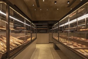 Modern bakery interior with glass display counters showcasing an assortment of freshly baked breads and pastries.