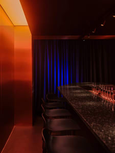 A sleek, metallic bar interior with black accents and a drink station featuring various bottles.
