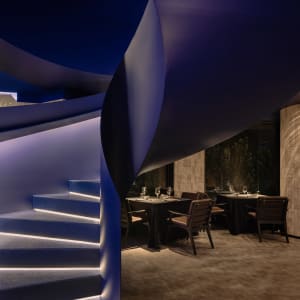 A modern restaurant interior featuring a curved, illuminated blue staircase.