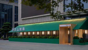 Modern restaurant exterior with a green metal roof and illuminated signs.