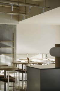 A modern restaurant interior featuring minimalist design, wooden tables, and concrete finishes.