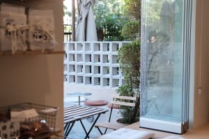 A modern cafe outdoor terrace featuring concrete blocks, glass walls, and wooden furniture.