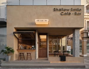 Shallow Smile Cafe Bar storefront with concrete exterior, wooden accents, and glass windows.