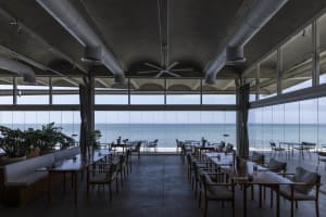 An industrial-style restaurant with a sea view, featuring concrete and glass materials.