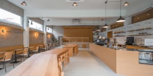 Interior of a minimalist coffee shop with wooden tables, chairs, and shelves, concrete walls, and a concrete floor.