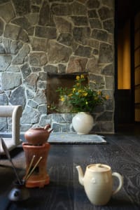 A cozy living room with a stone fireplace, wooden floor, and a white vase with yellow flowers.