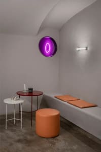 A minimalist living space with concrete walls, a white cushioned seat, and a purple illuminated object.