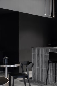 A modern cafe bar interior with black chairs, a grey high counter, and concrete walls.