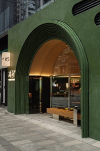 A modern storefront with a green concrete structure and a wooden bench inside.