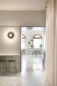 A minimalist commercial interior featuring a terrazzo floor with a modern light fixture and a bar area with stools.