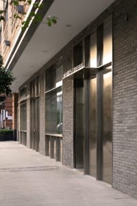 Retail storefronts with brick walls, glass windows, and metallic cladding on a city street.