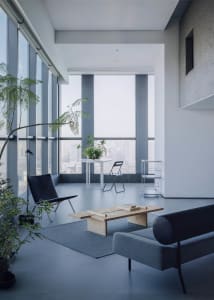 Modern minimalist living room with blue accents, featuring wooden coffee table, black leather chair, and large windows overlo