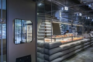 A bakery interior with a modern industrial design featuring glass, concrete, and canvas materials.