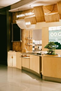 A modern restaurant interior featuring wooden and bamboo decor, with a counter and signage for Jincheng Tea.