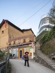 An old brick building sitting on a hillside street with a woman standing in front.