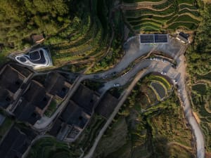 Aerial view of a terraced hillside village with winding roads and solar panels.
