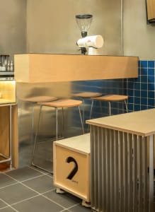 Modern wooden coffee shop bar counter with stools and espresso grinder.