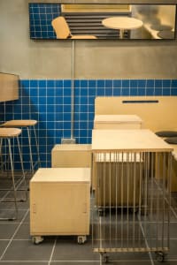 A minimalist cafe interior featuring wooden furniture and blue tiled walls.