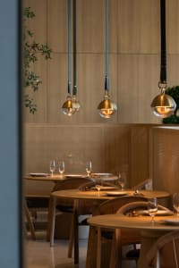 Modern restaurant dining room with wooden tables, chairs, and pendant lights.