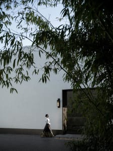 A woman wearing a black dress is walking towards a white wall with a black framed glass door.