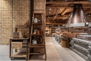 A modern bakery interior with a rustic wood theme featuring shelves, baskets, and a bread oven.