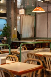 A rustic restaurant interior with wooden tables, metal railings, and green plants.
