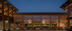 Outdoor area of a modern restaurant featuring bamboo and wooden structures, with tables and chairs arranged under a large roo