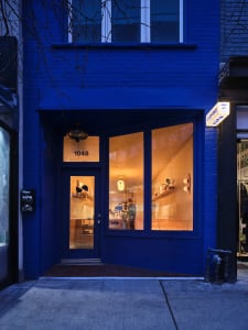 A blue storefront with large windows displaying a warm interior with lighting fixtures.