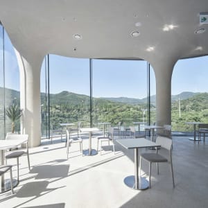 Modern restaurant interior with concrete and glass materials, featuring a minimalist design and open seating area.