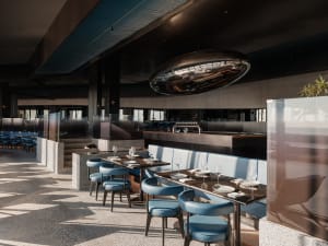 A modern, minimalist restaurant interior featuring metal, concrete, and leather materials.