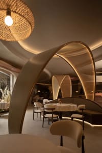 A modern restaurant with sleek, white walls, wooden tables, and fabric seating illuminated by soft lighting.