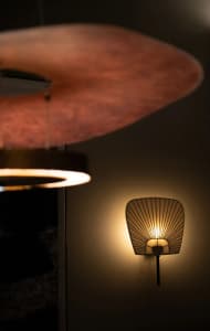 Modern lighting fixture with a shell-like design, featuring a metal base and glass shade emitting a warm glow.