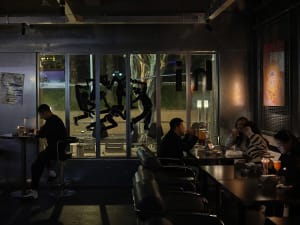 People sitting at tables in a modern metallic-themed cafe with large windows displaying outdoor scenery.