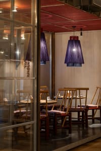An industrial-style restaurant interior featuring wooden tables and chairs with purple fabric lighting shades.
