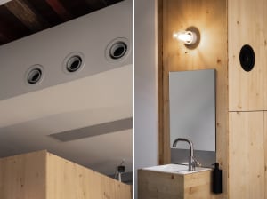 Modern minimalist bathroom with wood and metal elements, featuring a sink, mirror, and lighting fixtures.