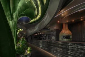 Interior view of a modern industrial restaurant with metallic glass bar counter and greenery.