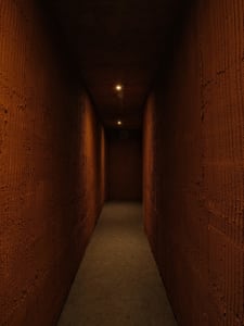 A minimalist tunnel corridor made of concrete, illuminated by two ceiling lights.
