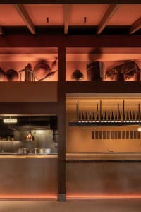 A modern, industrial restaurant bar with concrete, metal, and wood materials, featuring a wine bottle display and overhead li