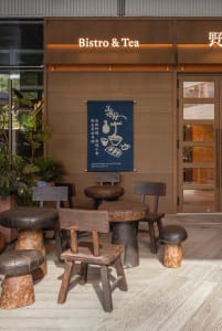 Industrial-style restaurant exterior with wooden tables, chairs, and stools.