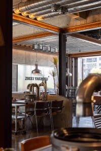 Industrial-style restaurant interior with exposed metal beams, concrete walls, and glass elements.
