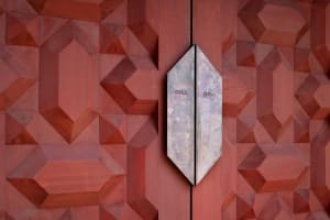 A close-up image of a red metal door featuring a geometric pattern.