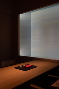 Minimalist dining room with wooden table and red napkin on a black placemat.
