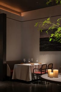 A minimalist restaurant interior featuring wooden tables, leather chairs, and a stone floor.