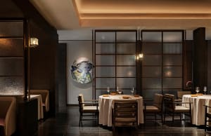A modern restaurant interior with a table setting featuring wine glasses, plates, and bowls on a round table covered in a whi