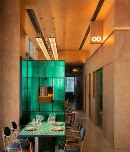 A modern restaurant interior features a green glass wall with a metallic accent and sleek, black chairs with metal frames.