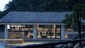 A minimalist restaurant with concrete walls and large windows, featuring modern furniture and a clean design.